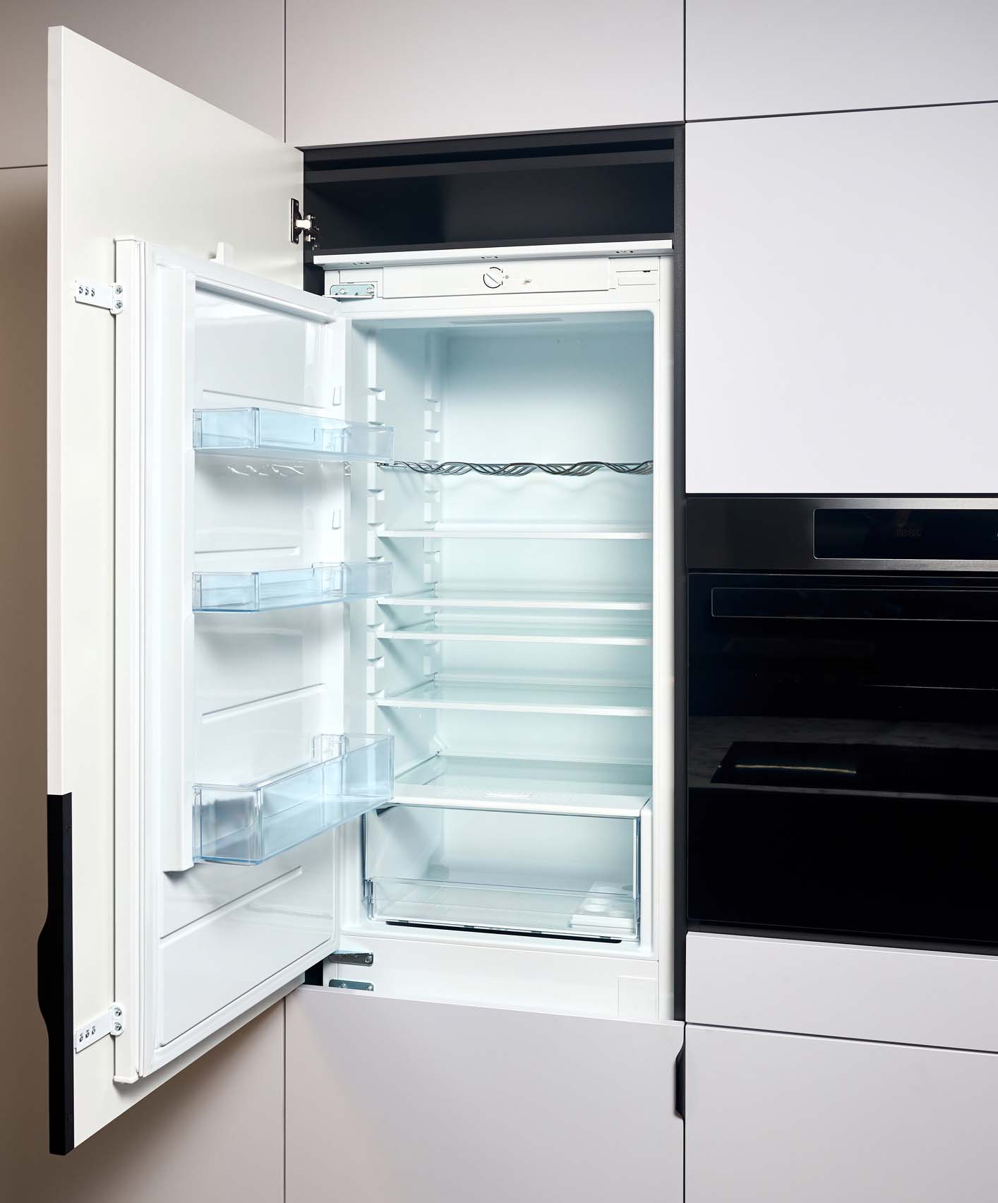 Vertical shot of kitchen interior with beige wooden furniture and modern appliances. Opened built integrated refrigerator with opened door empty shelves, stove, oven and black microwave oven in Belfast